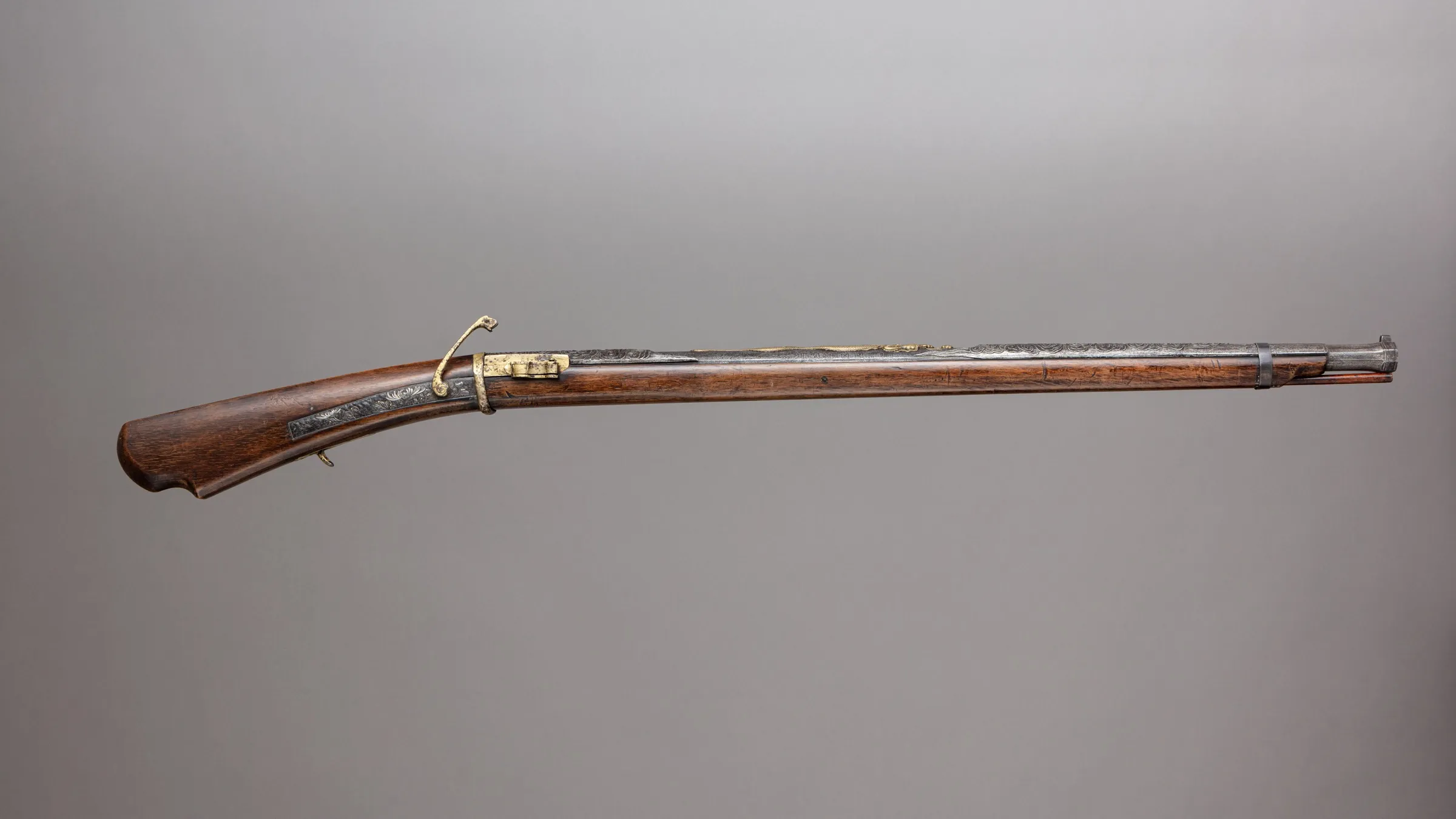 A long Japanese matchlock gun with a dark wooden stock, metal barrel, and brass firing mechanism photographed against a neutral grey background.
