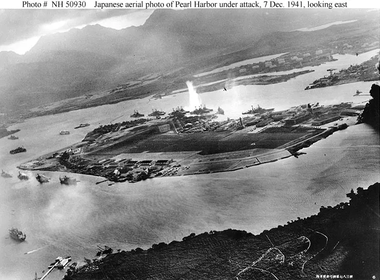 An oblique aerial photograph from a Japanese aircraft shows Ford Island, moored U.S. ships, aircraft, and a torpedo strike plume during the attack on Pearl Harbor.