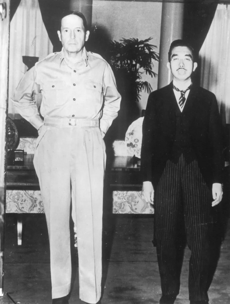 General Douglas MacArthur stands in a light open-collared uniform with his hands in his pockets beside Emperor Hirohito, who wears a formal dark suit at the U.S. Embassy in Tokyo.