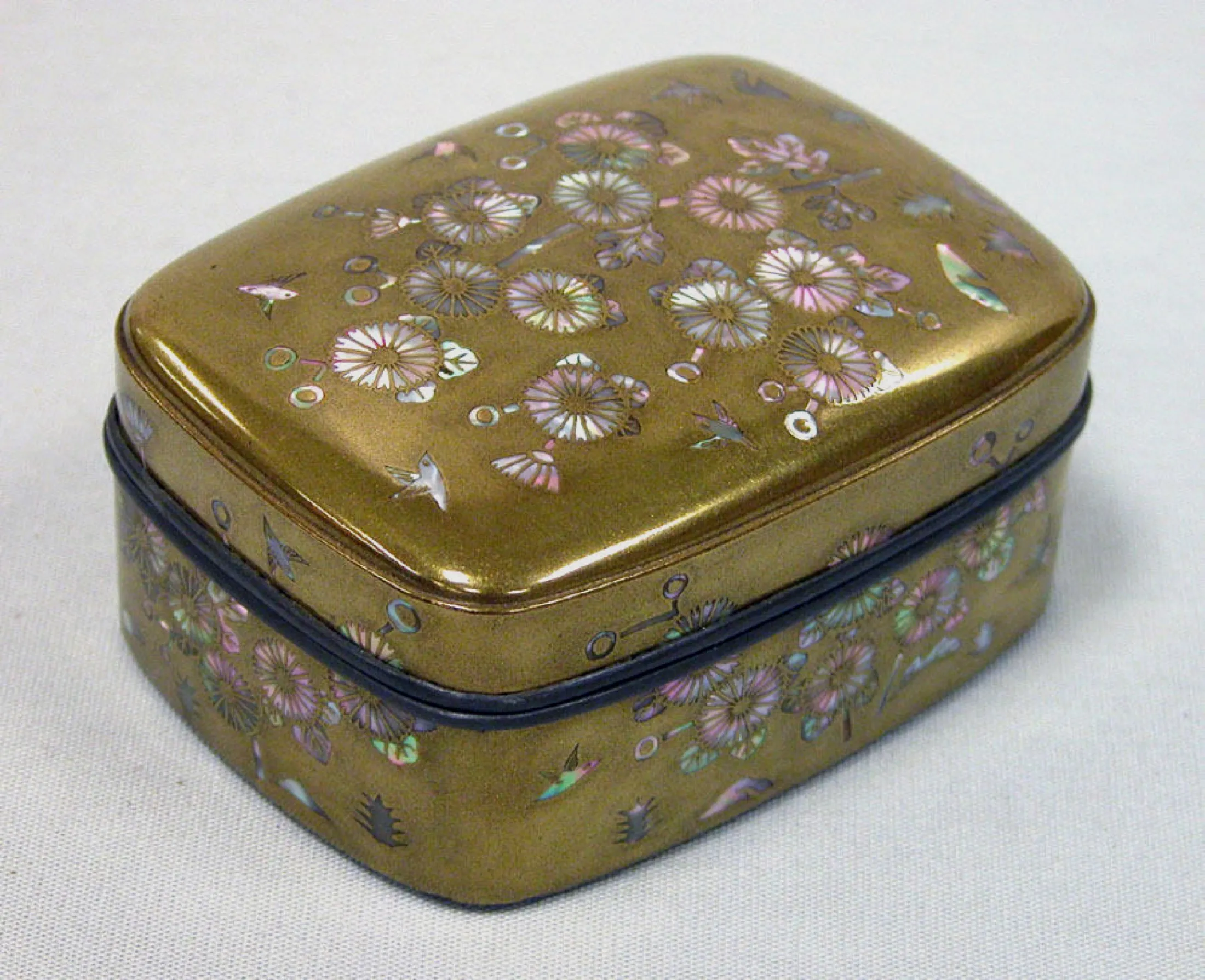 A small rounded gold lacquer incense box is densely decorated with iridescent mother-of-pearl flowers, leaves, and tiny birds.