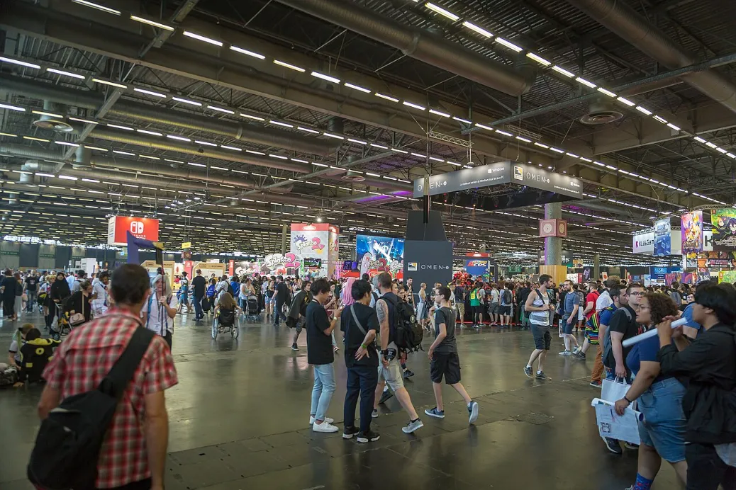 Visitors cross a large convention hall beneath Nintendo and game-franchise signs while queues form around booths at Japan Expo near Paris.